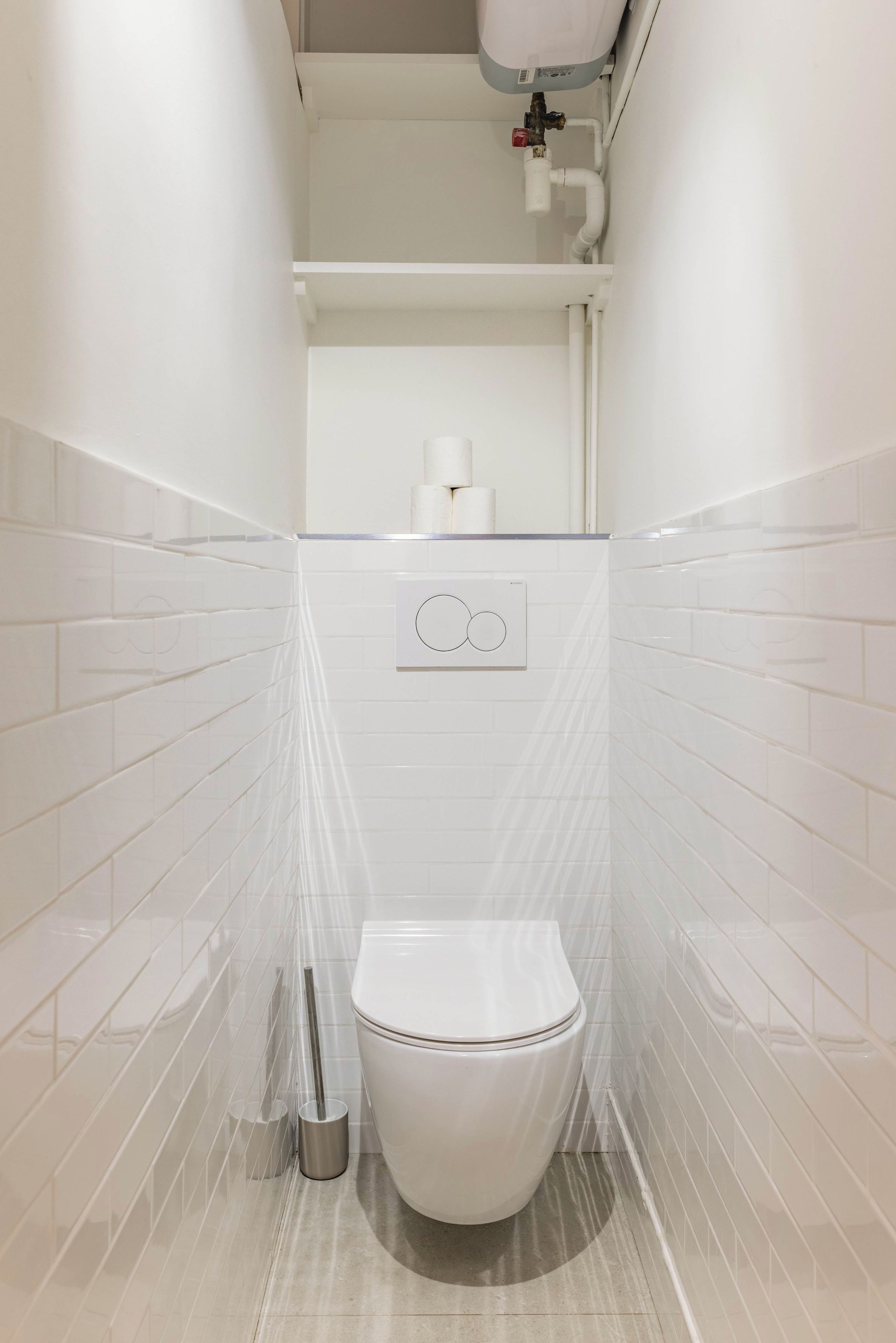 Een badkamer met een toilet, een hygiëneschuimer en een toiletrolhouder aan de muur.