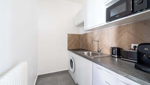 A compact kitchen with a microwave, toaster, and washing machine. - Studio Chic & Cosy au Cœur d'Issy (Issy-les-Moulineaux)