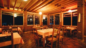 An indoor dining area with wooden tables and chairs, brick walls, and large windows. - ZONDELA HOUSE (Arusha)