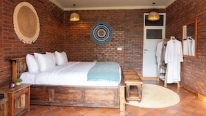 A room with a brick wall, a bed with white bedding, a wooden bench, and a small table. - ZONDELA HOUSE (Arusha)