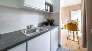 Una cucina moderna con mobili bianchi, un lavello in acciaio inossidabile e un forno a microonde. Sullo sfondo, una sedia gialla e un piccolo tavolo da pranzo.