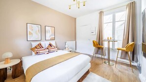 Camera d'albergo con un letto grande, una scrivania con due sedie, un lampadario e una finestra con tende.
