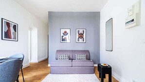 A modern living room with a sofa, a small table, and a chair. There are abstract paintings on the wall. - Appartement Cosy aux Portes de Paris (Issy-les-Moulineaux)