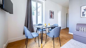 A modern living room with a dining area, featuring a sofa, a table with chairs, and artwork on the walls. - Appartement Cosy aux Portes de Paris (Issy-les-Moulineaux)
