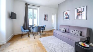 A modern living room with a sofa, a dining table with chairs, and a TV mounted on the wall. - Appartement Cosy aux Portes de Paris (Issy-les-Moulineaux)