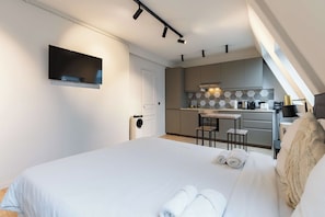A modern hotel room with a bed, a flat-screen TV, a kitchenette, and a view of the sky. - Cocon pour 2 personnes central - Beaubourg / Notre-Dame (Paris)