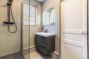 Ein modernes Badezimmer mit Duschkabine aus Glas, einem weißen Waschbecken und einem Spiegel darüber.