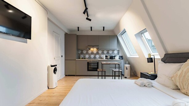 A modern bedroom with a large bed, a small kitchenette, and a window providing natural light. - Cocon pour 2 personnes central - Beaubourg / Notre-Dame (Paris)