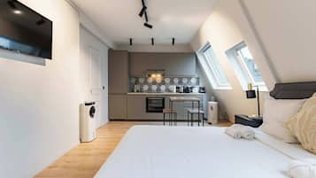 Une chambre moderne dotée d’un grand lit, d’une petite kitchenette et d’une fenêtre laissant entrer la lumière naturelle.