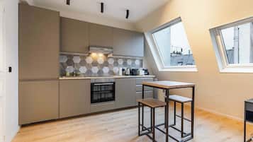 A modern kitchen with a built-in oven, a small dining table, and a window providing a view of the cityscape.