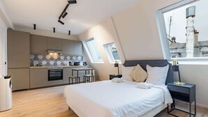 A modern bedroom with a large bed, a nightstand, and a view of the city through a window. - Cocon pour 2 personnes central - Beaubourg / Notre-Dame (Paris)