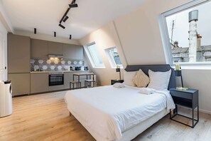Ein modernes Schlafzimmer mit einem großen Bett, einem Nachttisch und Blick auf die Stadt durch ein Fenster.