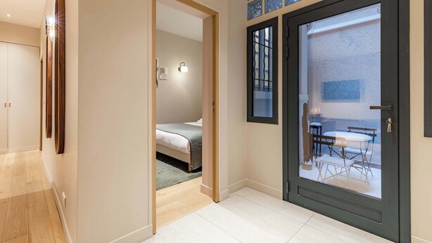 Ett hotellrum med en säng, ett litet bord och en stol. Det finns en dörr som leder ut till en balkong med utsikt över omgivningen.
