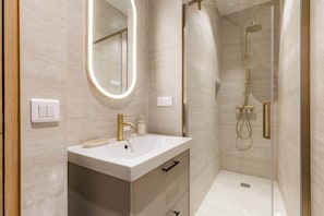A modern bathroom with a white sink, gold fixtures, a large mirror, and a glass-enclosed shower area. - Grand 4 pièces climatisé avec patio à Paris (Paris)