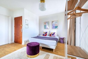 A modern bedroom with a bed, a purple ottoman, a wooden door, and abstract wall art. - Charmant studio équipé près de Mairie d'Issy (Issy-les-Moulineaux)