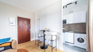 A compact living space with a kitchenette, a dining area with two chairs, a sofa, and a washing machine. - Studio chaleureux au coeur de ville Issy (Issy-les-Moulineaux)