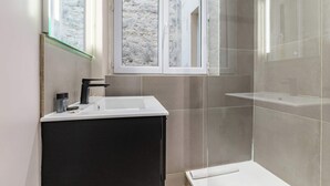 Une salle de bain moderne avec un lavabo blanc, un meuble sombre et une cabine de douche en verre.