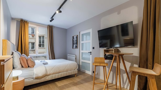 Une chambre moderne avec un lit, un bureau, une chaise, une télévision et une fenêtre avec des rideaux.