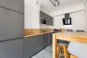 A modern kitchen with grey cabinets, a wooden countertop, and a dining area with a table and chairs. - Grand appartement 80m2 2BR - Beaubourg / Notre-Dame (Paris)