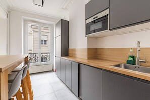 A modern kitchen with grey cabinets, a wooden countertop, and a built-in oven. - Grand appartement 80m2 2BR - Beaubourg / Notre-Dame (Paris)