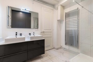 A modern bathroom with two sinks, a large mirror, and a walk-in shower. - Grand appartement 80m2 2BR - Beaubourg / Notre-Dame (Paris)