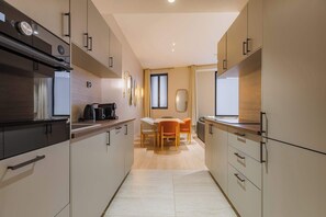 Eine moderne Küche mit Essbereich, ausgestattet mit hellen Holzschränken, einer zentralen Kochinsel und Blick zum Wohnzimmer.