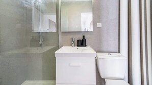 Une salle de bain moderne avec une douche à parois de verre, un lavabo blanc avec un miroir au-dessus et des toilettes.