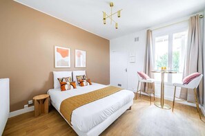 Une chambre d’hôtel moderne avec un grand lit, une petite table ronde, deux chaises et une fenêtre avec des rideaux.