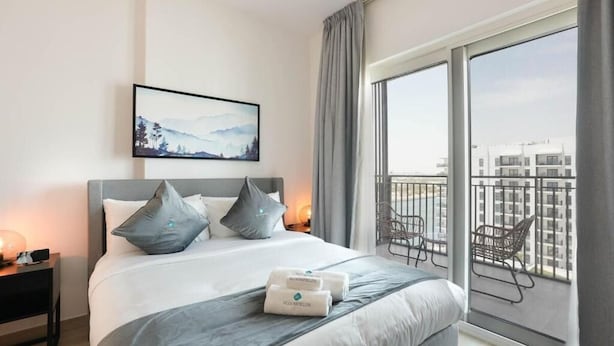 A modern hotel room with a large bed, grey bedding, a city view balcony, and a framed picture on the wall. - Bloomfields STU Canal View Waters Ed 1 (Abu Dhabi)