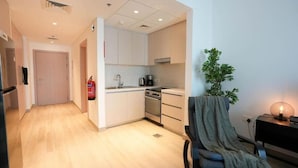 A compact kitchen with modern appliances, a bench with a blanket, and a potted plant. - Bloomfields STU Canal View Waters Ed 1 (Abu Dhabi)