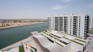 A modern high-rise building with a river in the background. - Bloomfields STU Canal View Waters Ed 1 (Abu Dhabi)