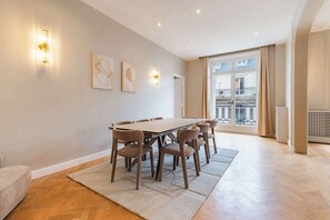Ein geräumiger Raum mit großem Esstisch und Stühlen, einer Couch und Blick auf einen Balkon mit Geländer.