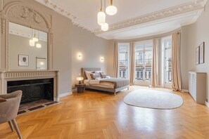Ein geräumiges Schlafzimmer mit einem großen Bett, einem Kamin und Blick auf die Stadt durch große Fenster.