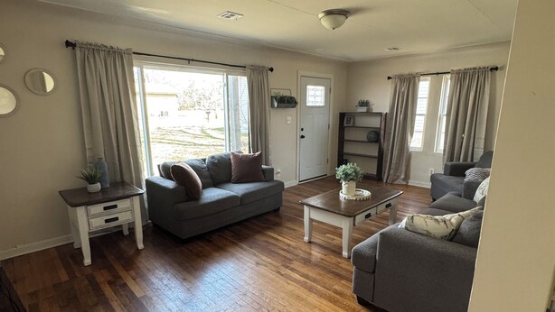 A spacious living room with hardwood flooring, two grey sofas, a coffee table, and a door leading outside.