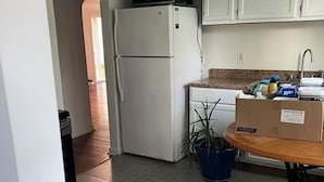 A compact kitchen with white cabinets, a refrigerator, a microwave, a sink, and a potted plant.