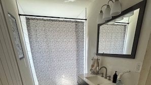 A bathroom with a patterned floor, a toilet, a sink with a mirror, and a shower curtain.