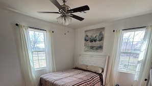A bedroom with a bed, a ceiling fan, and two windows with curtains.