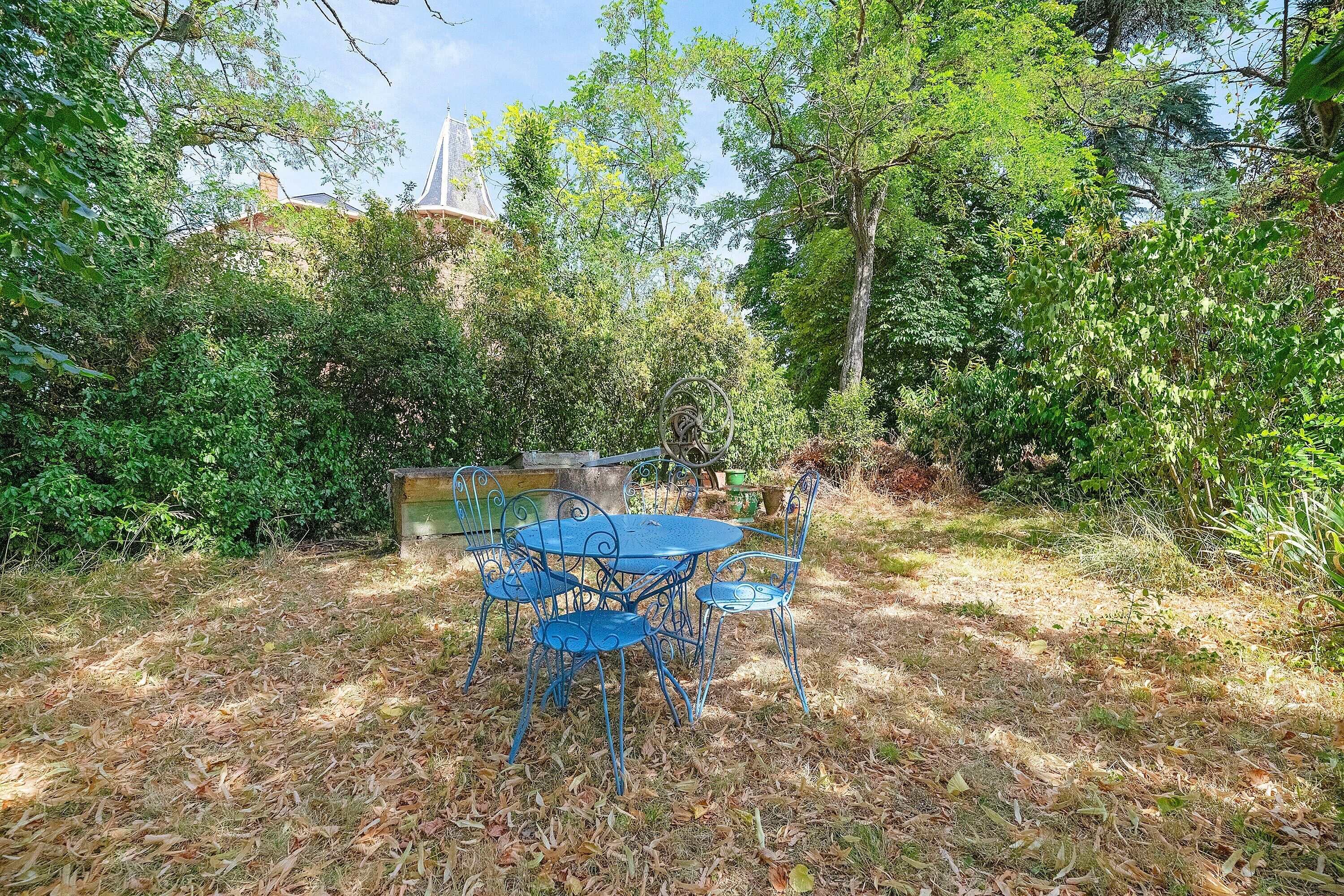 A blue metal table and chairs set in a garden with dense foliage and a stone structure in the background.