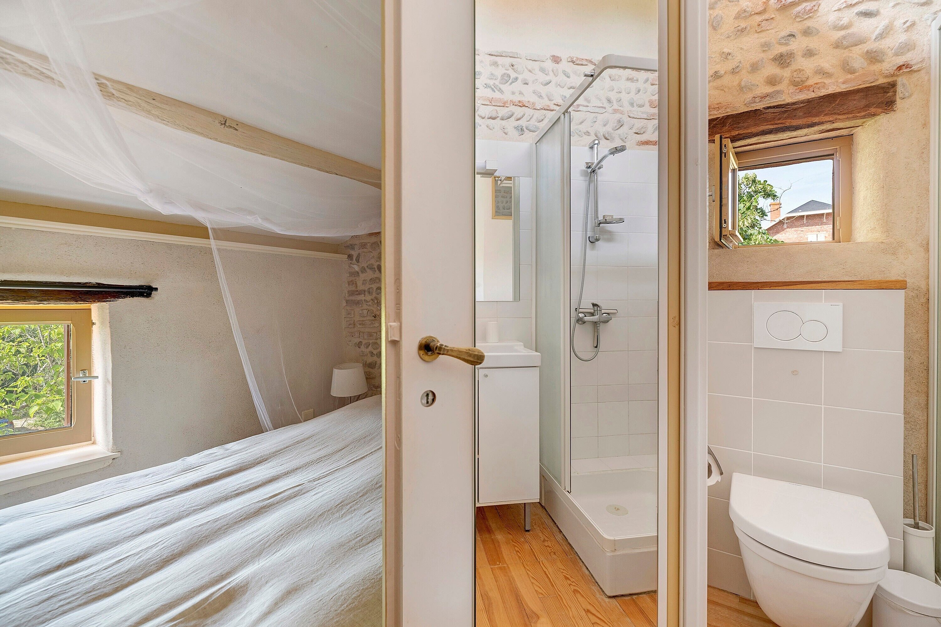 A room with a bed, a bathroom with a shower, and a toilet.