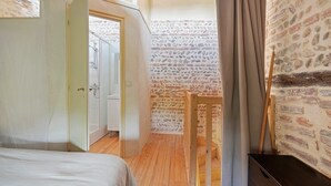 Ein Schlafzimmer mit Holzboden, einem Bett, einem Holzstuhl und einer Steinwand.