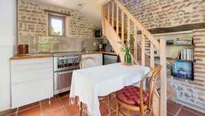 Eine Küche mit Herd, Backofen und Spüle, ein Esstisch mit Stuhl und eine Holztreppe.