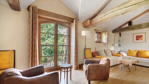 A living room with a sofa, chairs, a small table, a lamp, and a window with curtains.