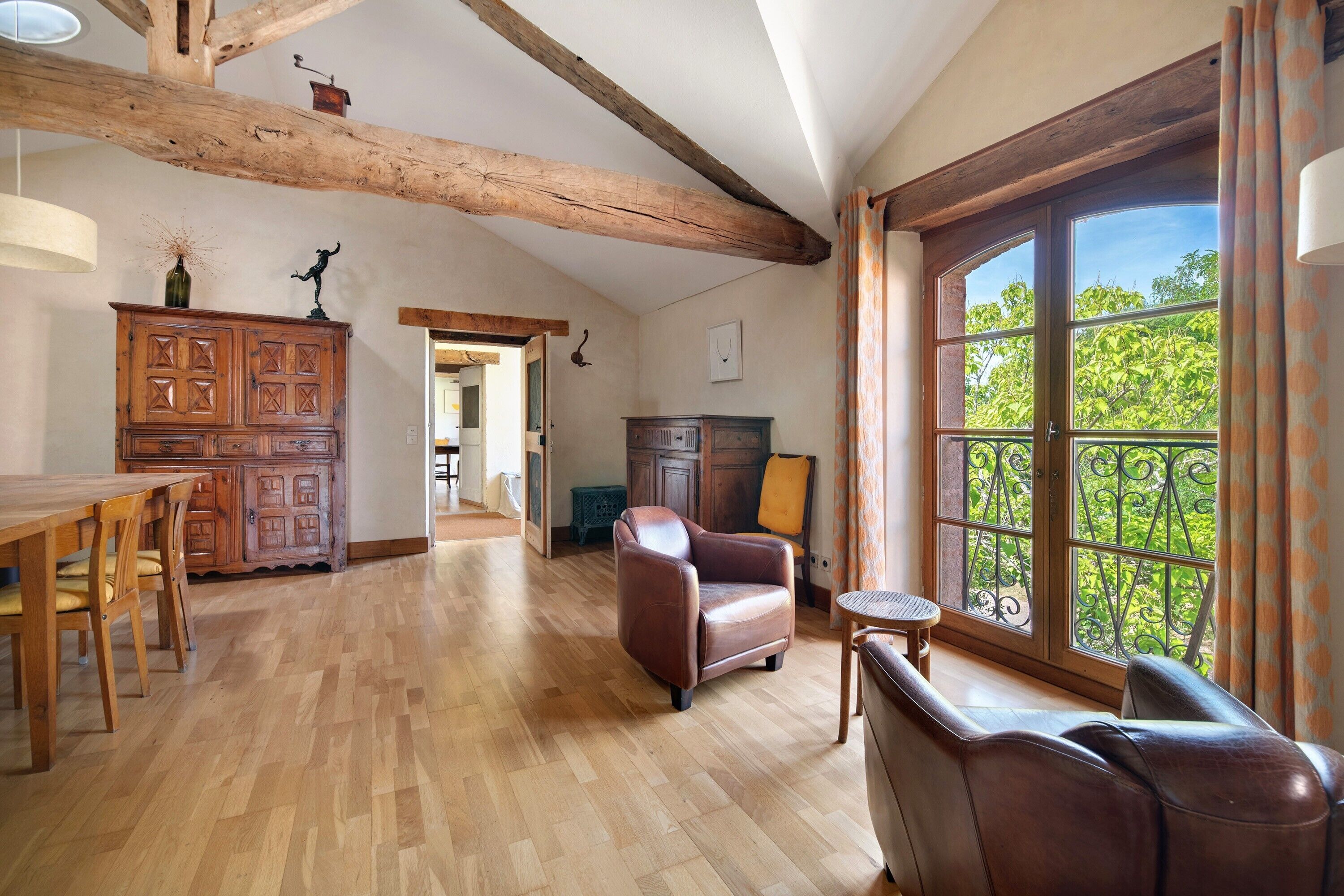 Quarto espaçoso com mesa de jantar de madeira, poltronas de couro e uma grande janela com vista para o verde.
