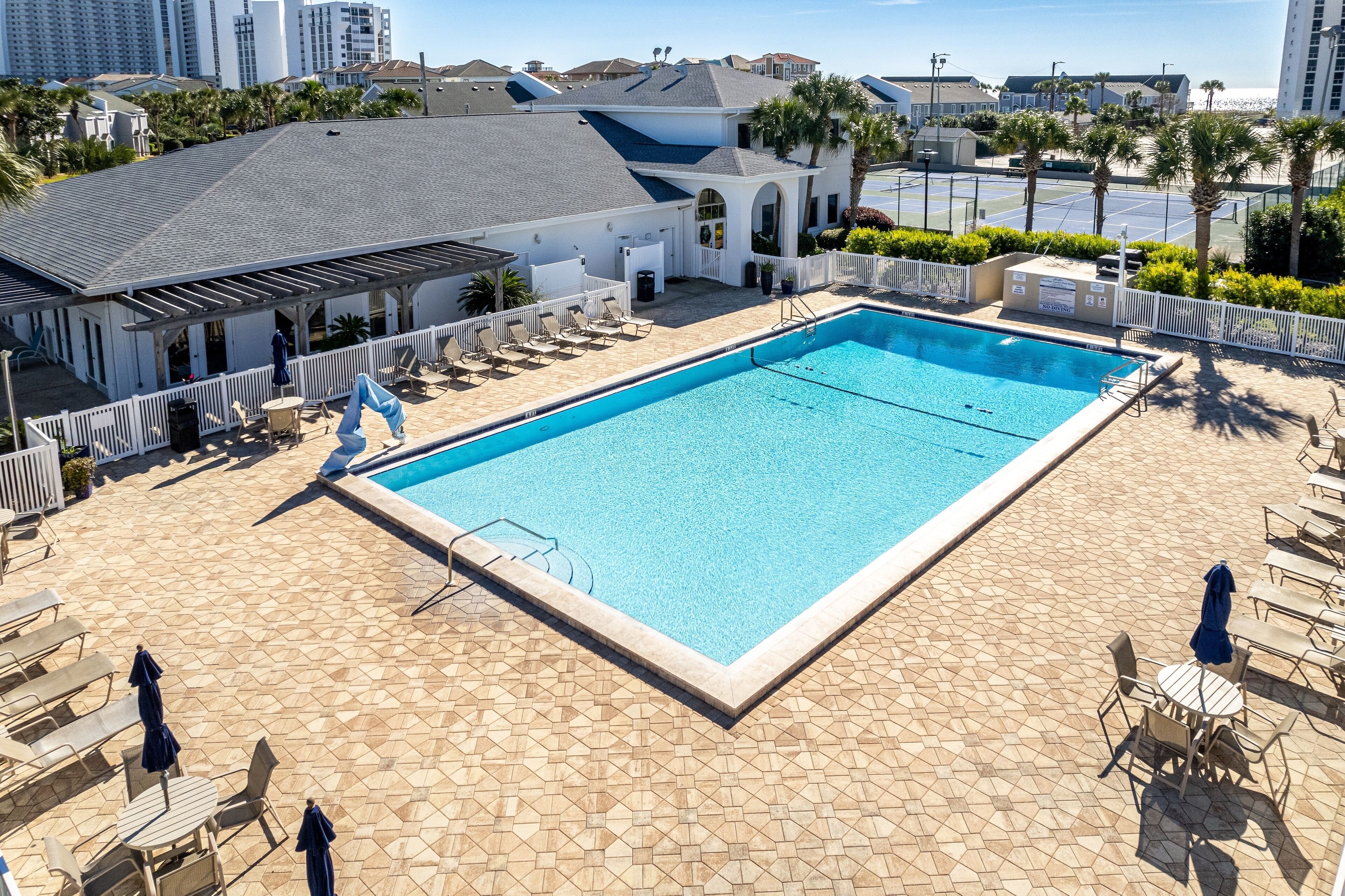 Ein rechteckiger Swimmingpool mit gefliestem Sonnendeck, umgeben von Liegestühlen und Sonnenschirmen.