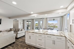 Eine moderne Küche mit weißen Schränken und einer Marmorarbeitsplatte, ein Essbereich mit Tisch und Stühlen sowie ein Wohnzimmer mit Sofa und Fernseher.