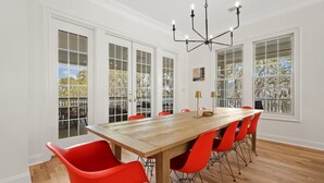 A dining room with a wooden table, red chairs, white walls, and large windows. - Dieu Not Disturb 5 Bedroom Home (Georgetown)