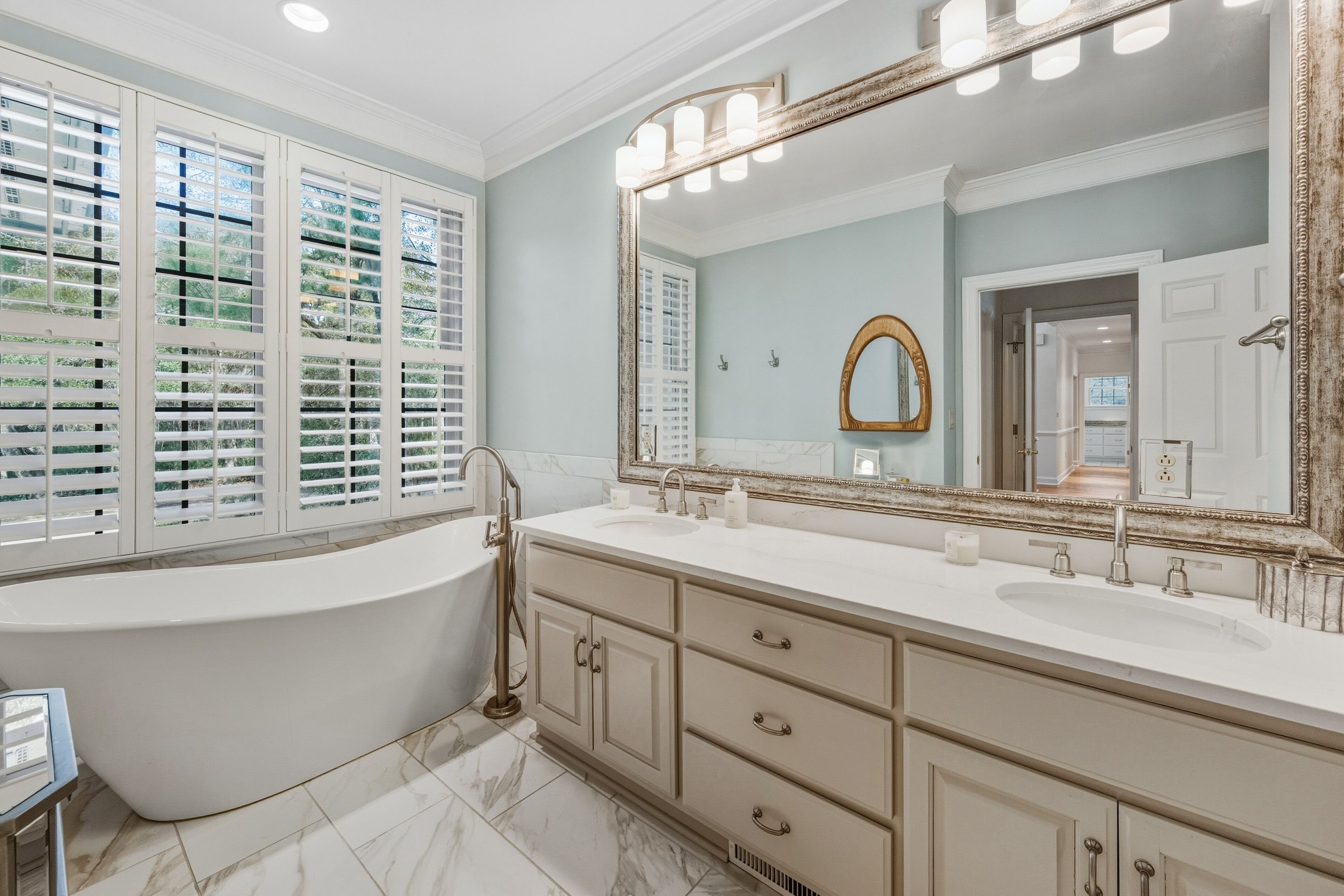 A bathroom with a freestanding bathtub, a large mirror, and a window with blinds.