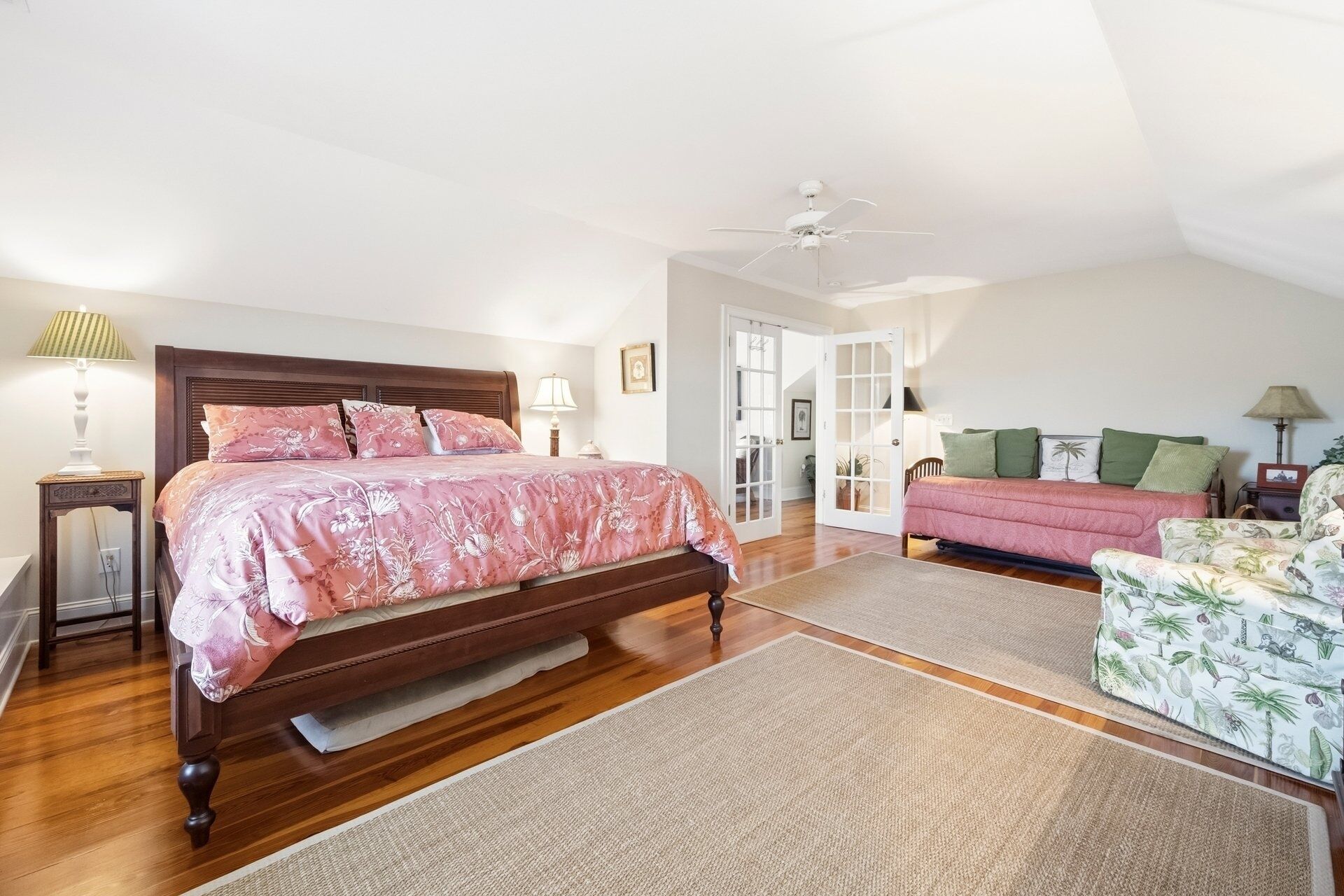 A bedroom with a wooden bed, a ceiling fan, a sofa, and a chair.
