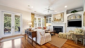 A spacious living room with a fireplace, a television, and a balcony with outdoor furniture. - Knock On Wood 5 Bedroom Home (Georgetown)