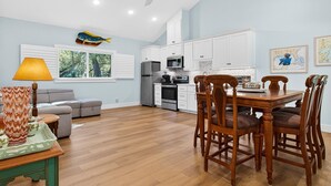 Una cucina moderna con mobili bianchi, un frigorifero in acciaio inossidabile e un'area pranzo con tavolo e sedie in legno.